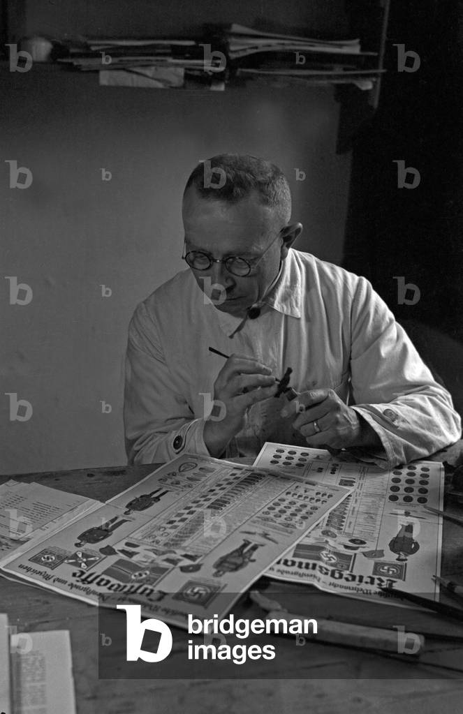 A painter decorating little porcellain sculptures of soldiers at the factory at Graefenthal, Thuringia, Germany 1930s (b/w photo)