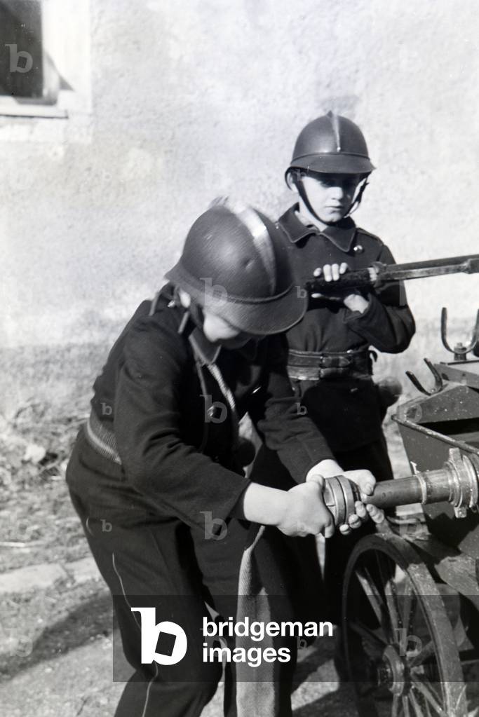 Two uniformed boys of the junior firefighters are installing the water hose during a firefighter training, Germany 1930s (b/w photo)