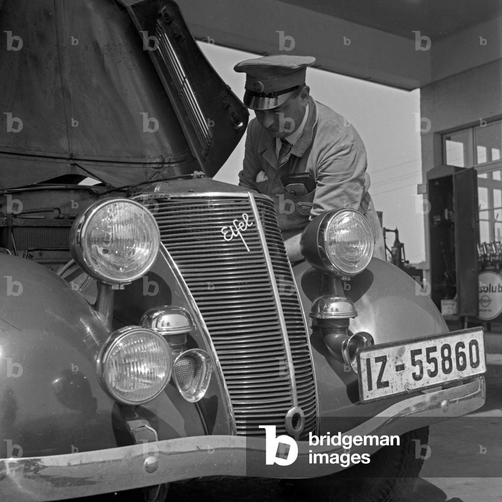 A filling station attendant checking the engine of a Ford model Eifel, Germany 1930s (b/w photo)