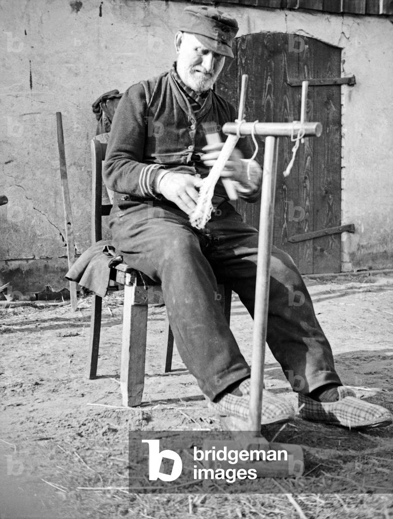 An old fisherman repairing his net, East Prussia, 1930s (b/w photo)