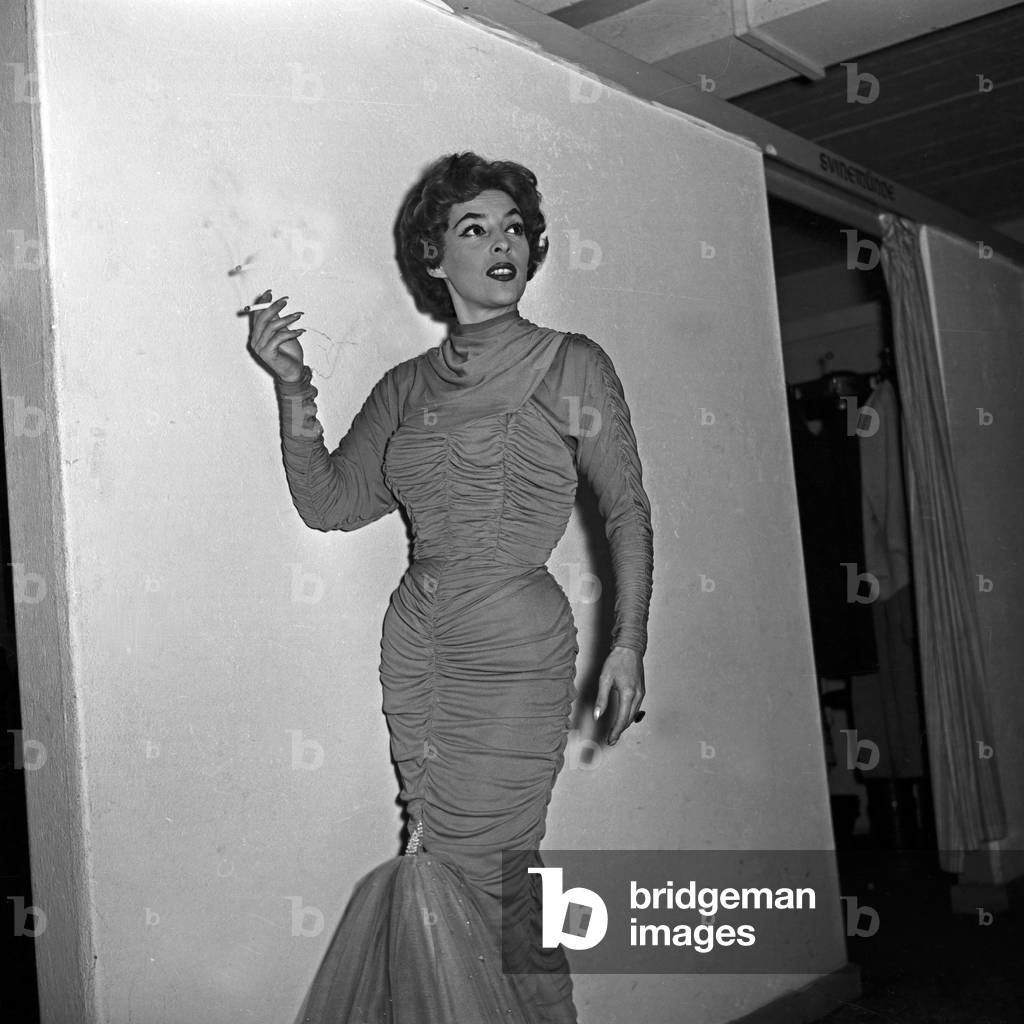 Singer in gala robe with a cigarette in front of a white wall at Hamburg, Germany 1950s