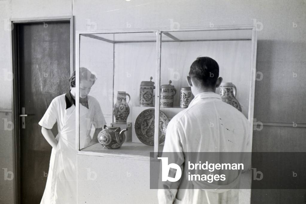 Two students of the College for Ceramics in Höhr-Grenzhausen looking at the ceramics exhibited in the hallway of the school, Germany 1930s (b/w photo)