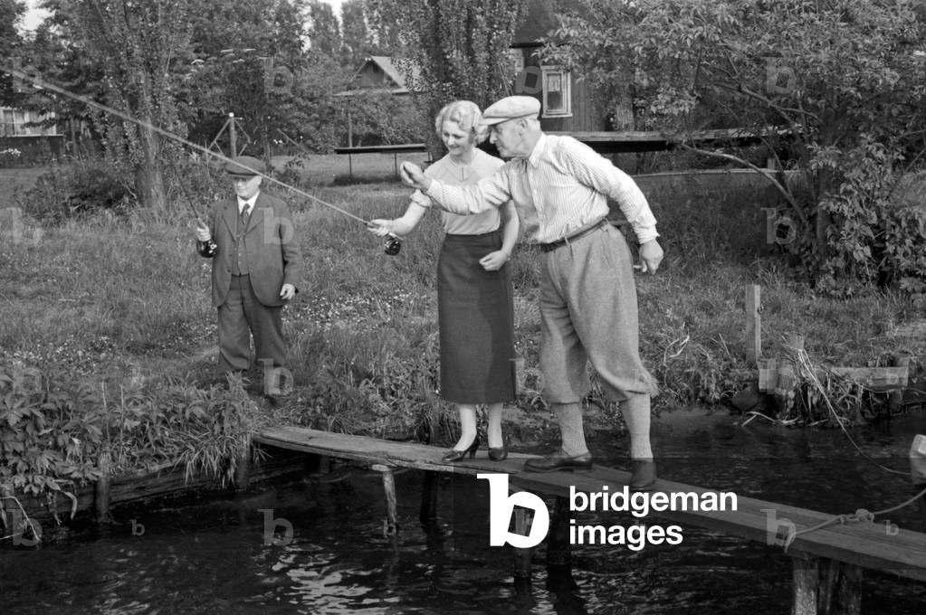 A woman listening and learning from her male competitors at an angling contest, Germany 1930s (b/w photo)