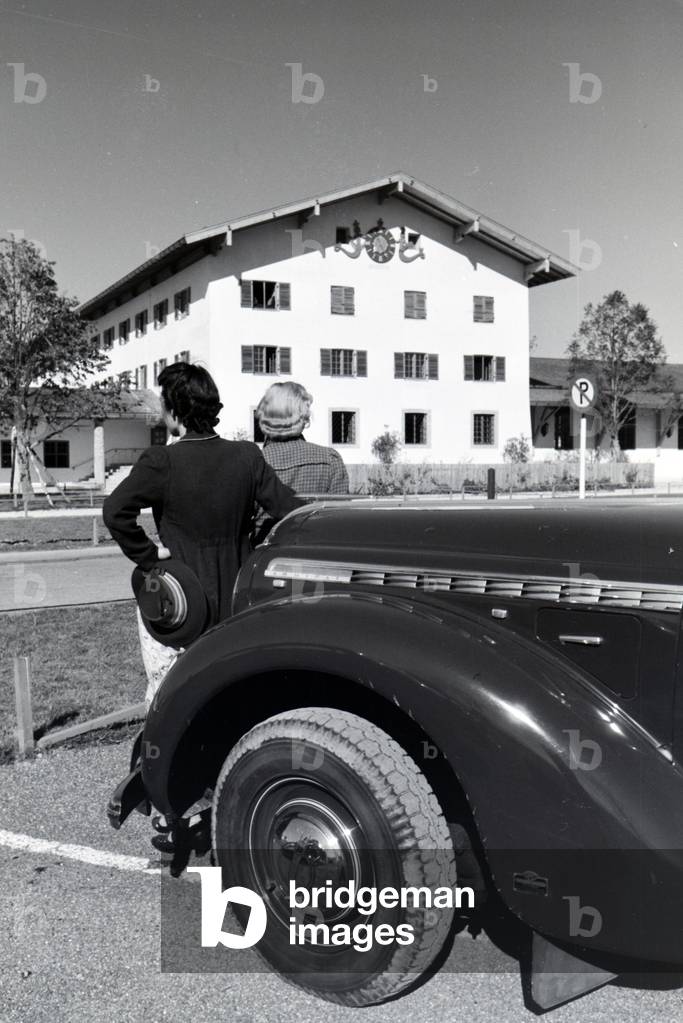 Two young women are looking at the clock on the wall of the city hall at the Chiemsee, Germany 1930s (b/w photo)