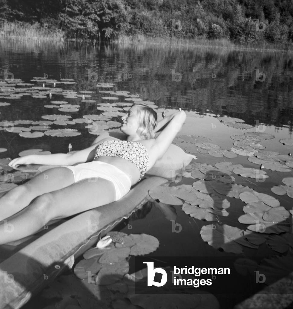A young woman on an air matress on a lake in the Wachau area in Austria, Germany 1930s (b/w photo)