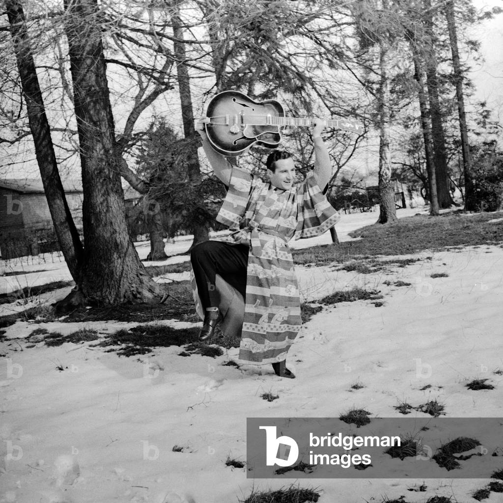 German singer Freddy Quinn dancing with his guitar in the snow, ca 1957