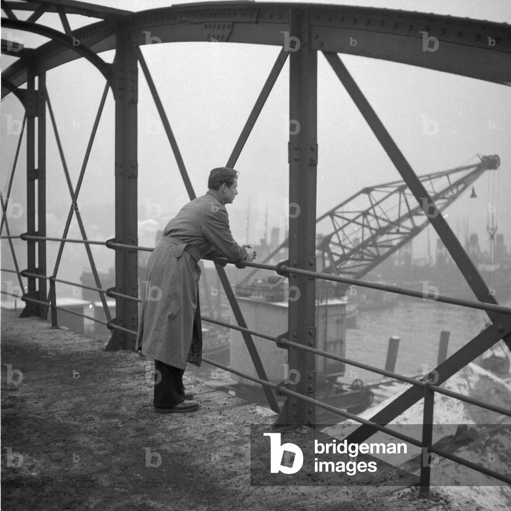 Ayoung man standing on a bridge and watching the Hamburg cargo harbor, 1954
