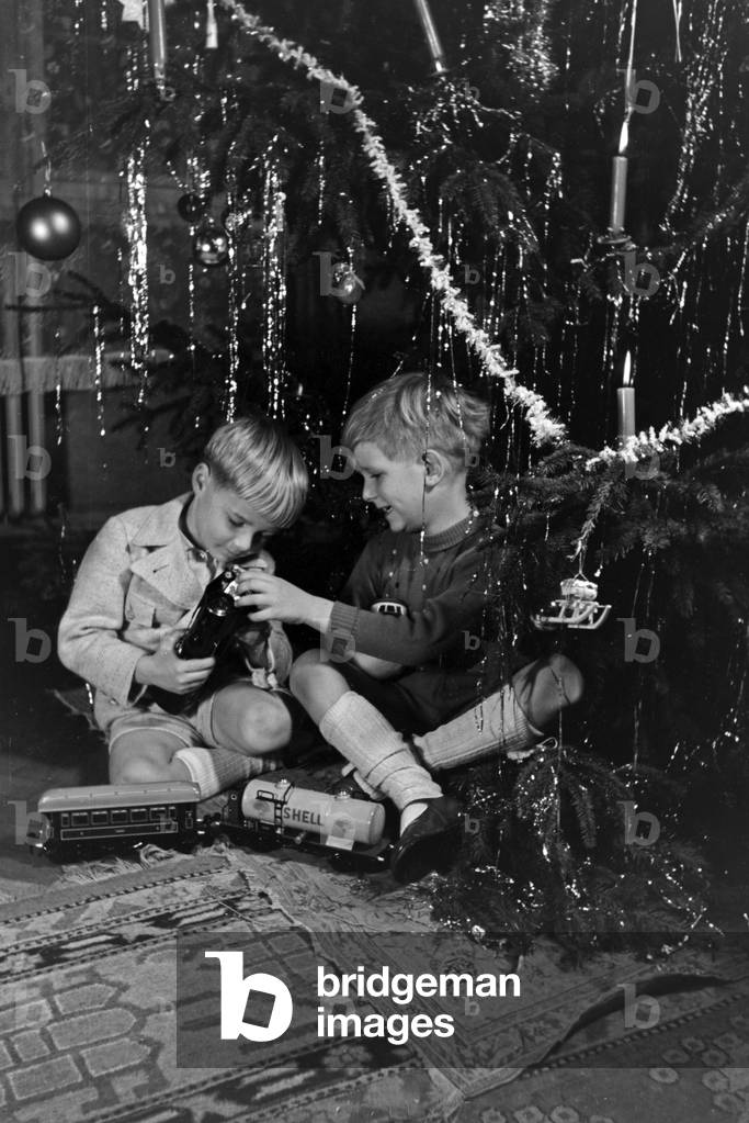 Two boys playing with the new model train under the christmas tree, Germany 1930s (b/w photo)