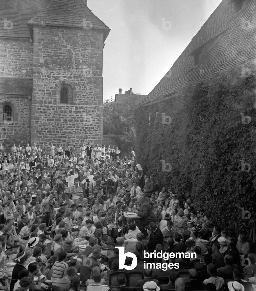 A German author (desk) is surrounded by the audience at poet's meeting in Lippoldsberg, Hesse, 1930s (b/w photo)
