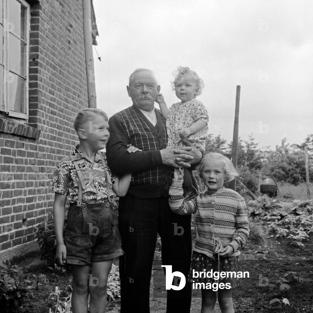 A proud grandafther with his grandchildren in the garden, Germany 1950s