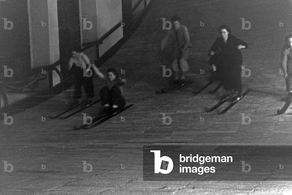 A group of skiing beginners learning how to ski at the woodden floor of a skiing hall, Germany 1930s (b/w photo)