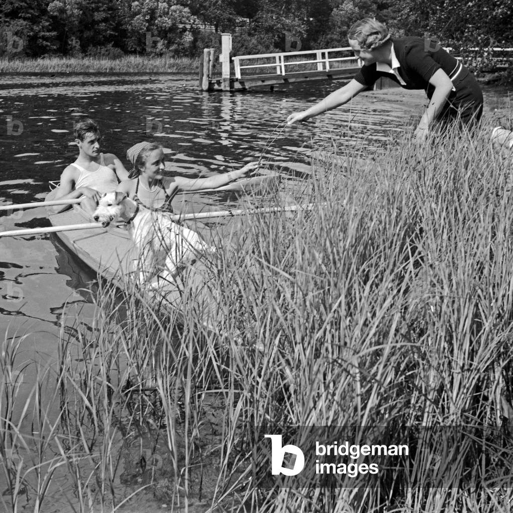 A man and a woman in a Klepper folding boat are welcomed by another woman on the shore of a lake, Germany 1930s (b/w photo)