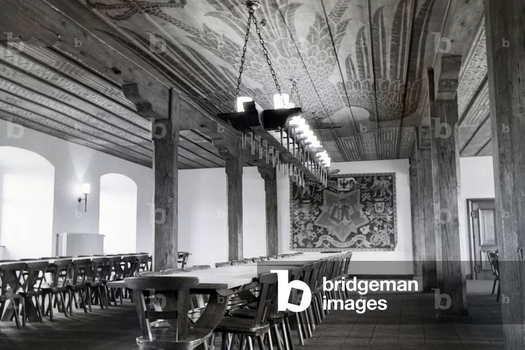 View of a hall with a long table, chandelier and decorations, imperial eagle, eagle motive on the wooden ceiling and tapestry, picture hanging on the wall, Germany 1930s (b/w photo)