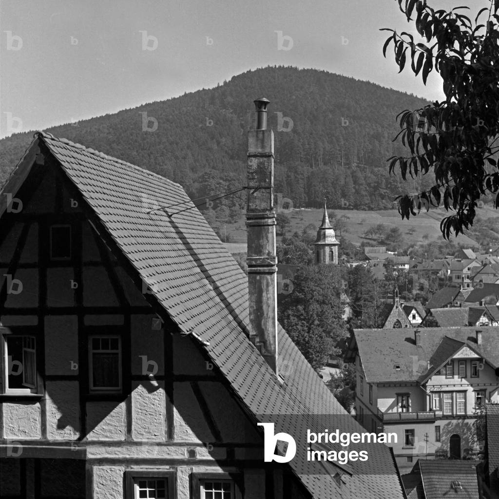 View to the belfry of the minster behind a timbered house at Herrenalb in Black Forest, Germany 1930s (b/w photo)