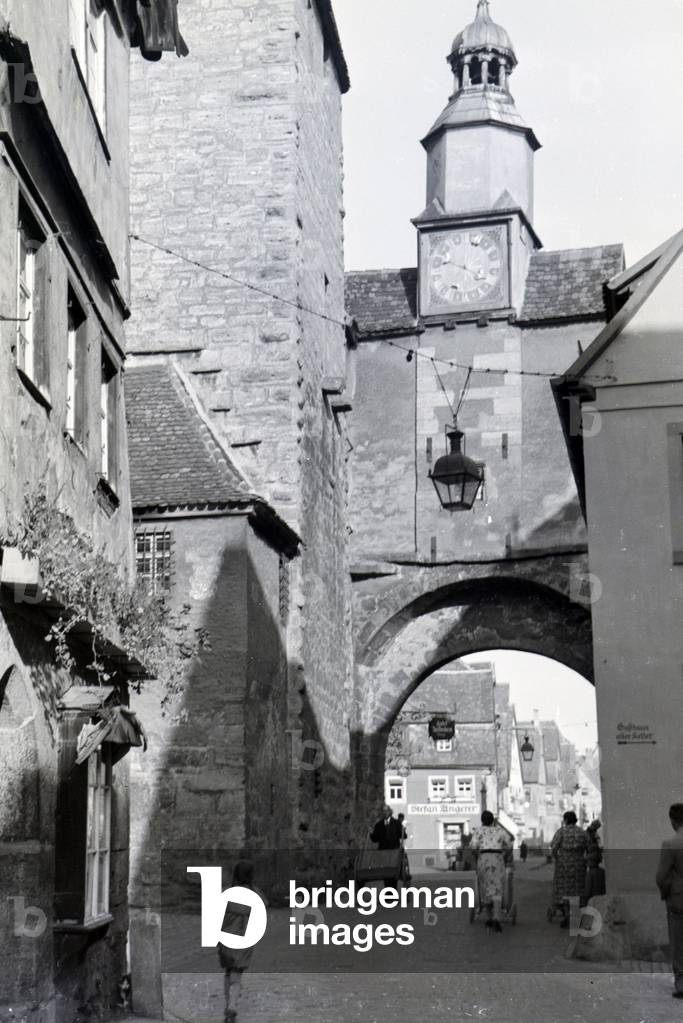 A hustle and bustle on a street with one of the many towers and archways in Rothenburg ob der Tauber, Germany 1930s (b/w photo)