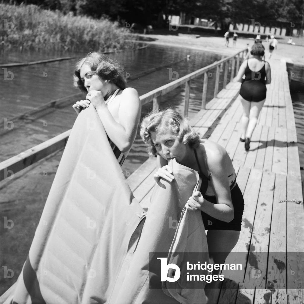 Two young women blowing up their air matresses on a lake in the Wachau area in Austria, Germany 1930s (b/w photo)