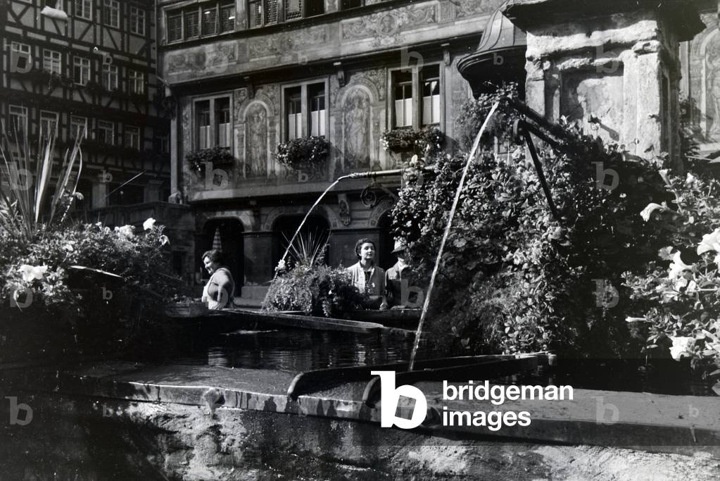 Besides the townhall, the fountain decorated with flowers is another object of interest at the market square in Tübingen, Germany 1930s (b/w photo)