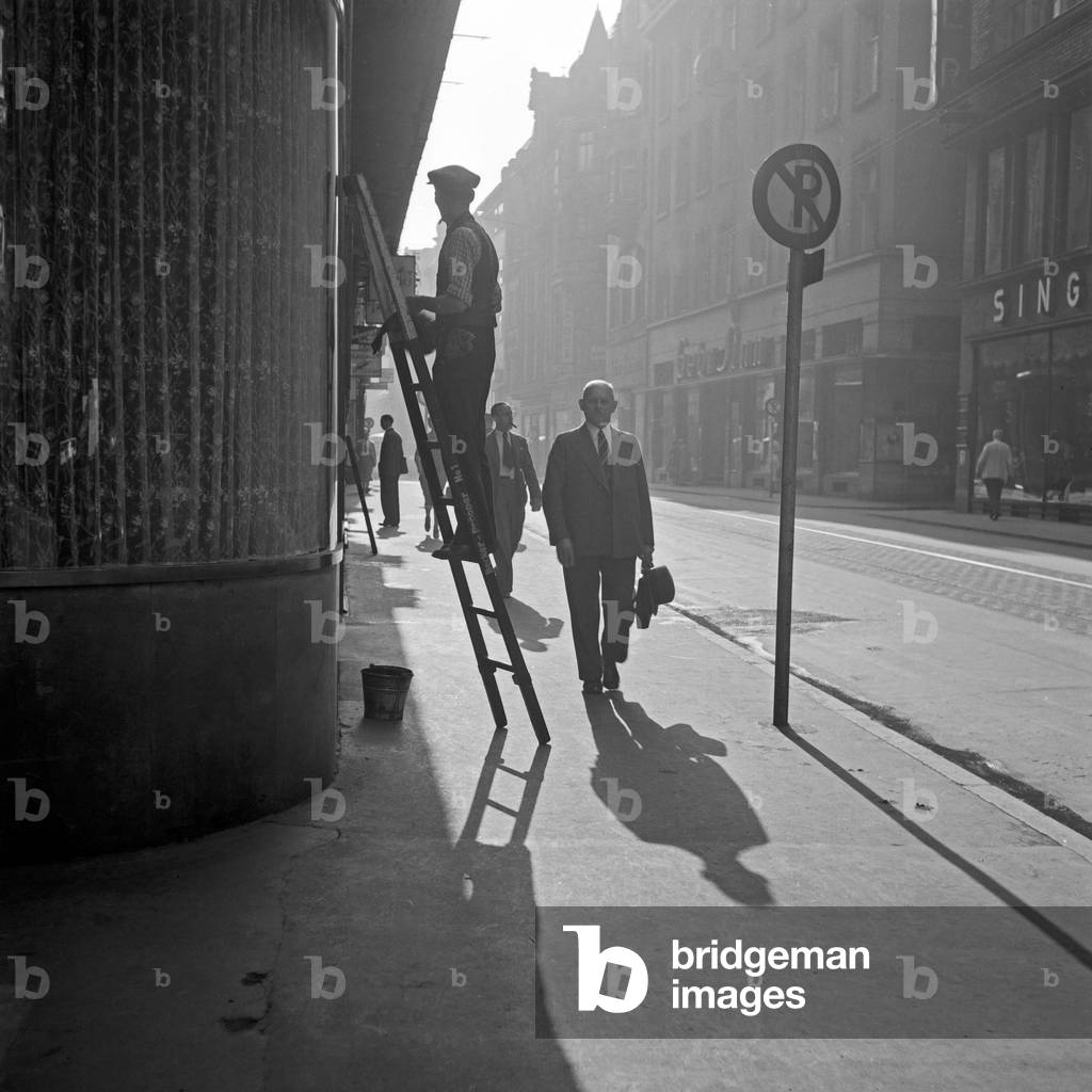 Passers by on their way see a window cleaner at the city centre of Dortmund, Germany 1930s (b/w photo)