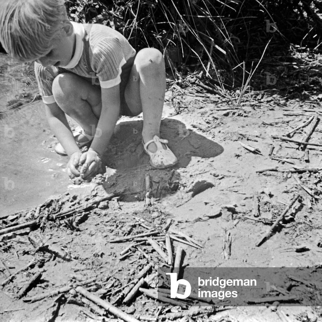 A little boy playing dedicativly in the mud, ruining his Sunday suit, Germany 1930s (b/w photo)
