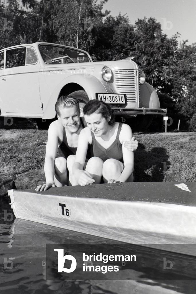 Young couple sitting in front of a boat at the river of a lake, Germany 1930s (b/w photo)