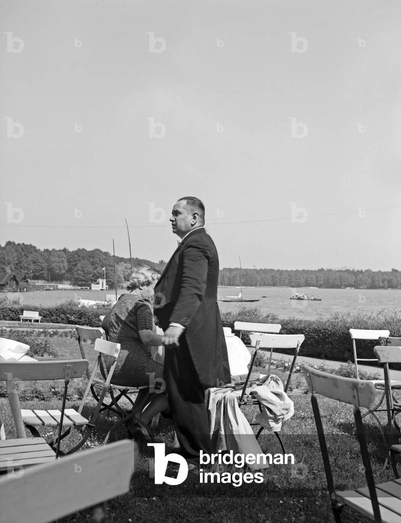 A waiter in a swallow tailed coat serving a lady at an open air restaurant, Germany 1930s (b/w photo)
