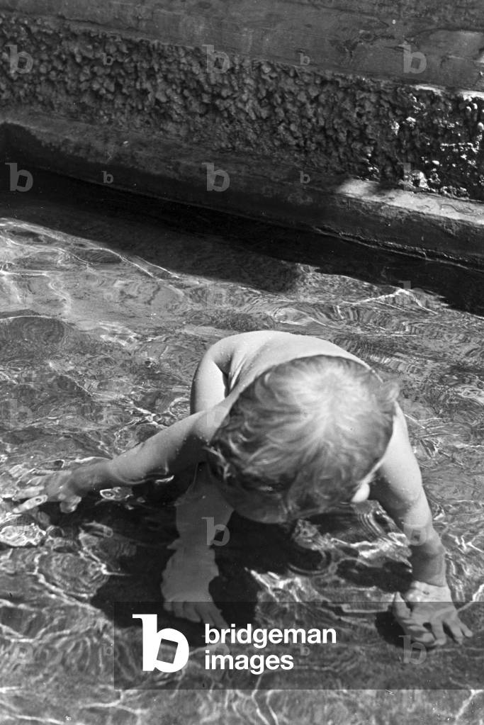 A playing toddler in the open-air swimming pool on a hot summer day, Germany 1930s (b/w photo)