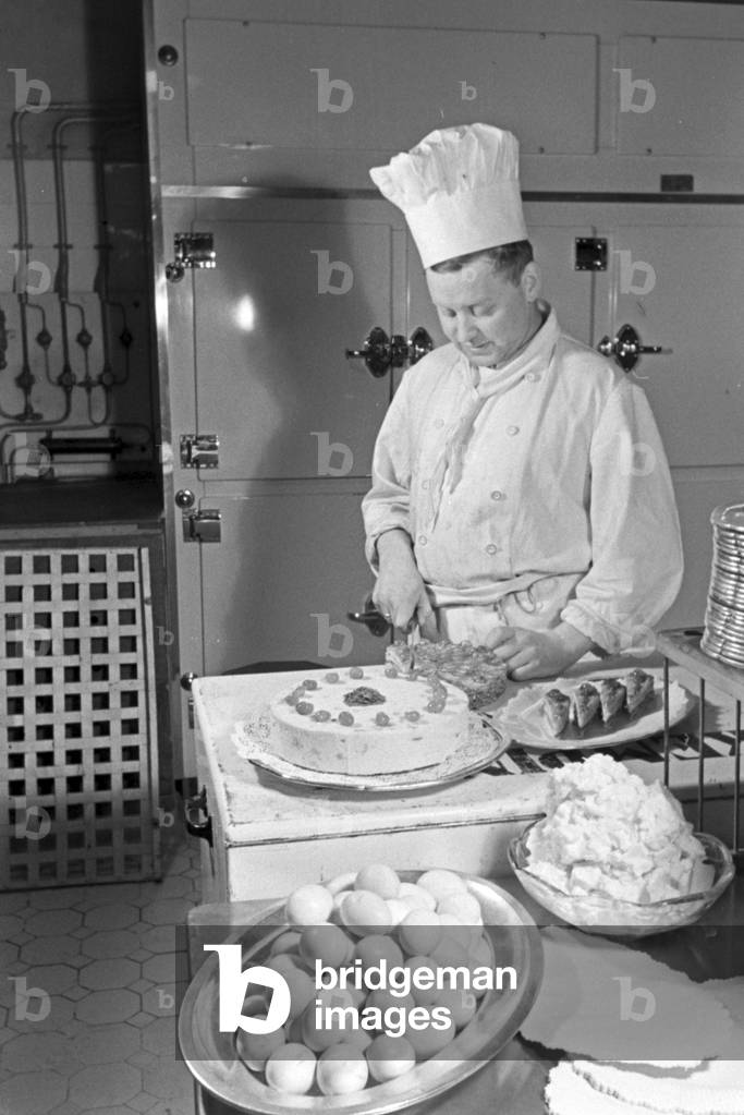 A pastry chef preparing desserts and cakes at the kitchen of a restaurant, Germany 1930s (b/w photo)