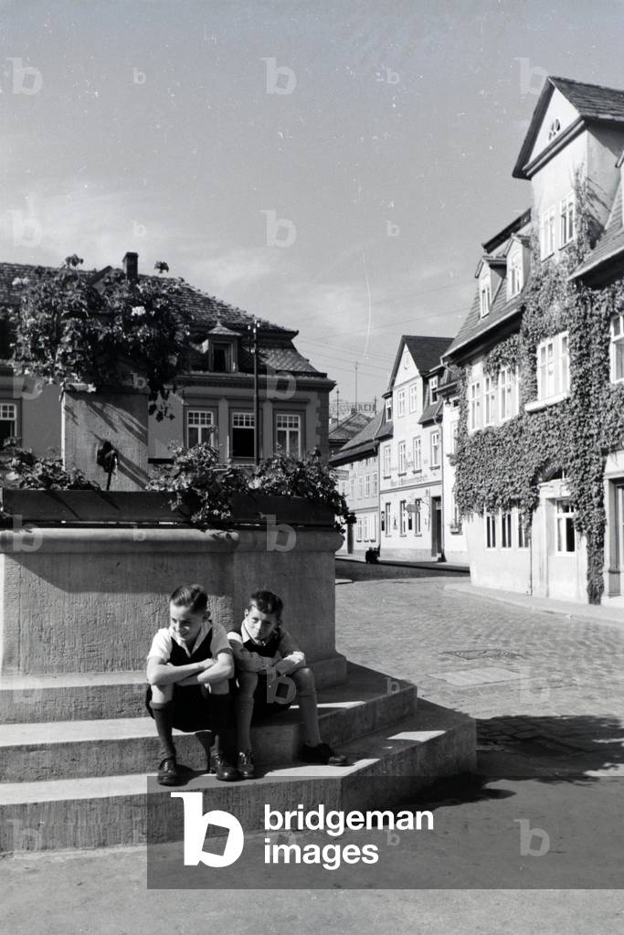 Two boys sitting at the fountain on the market square of Bad Blankenburg, Germany 1930s (b/w photo)
