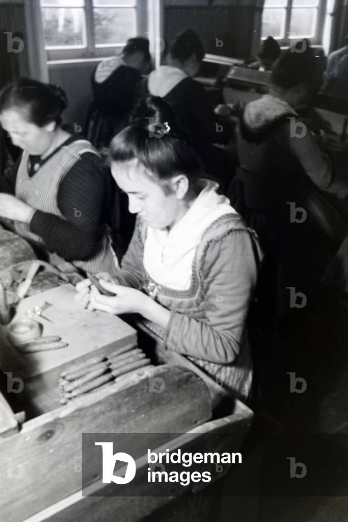 A female cigar roller wearing a Marburg garb, costume at work in a cigar fabric near Marburg, Germany 1930s (b/w photo)