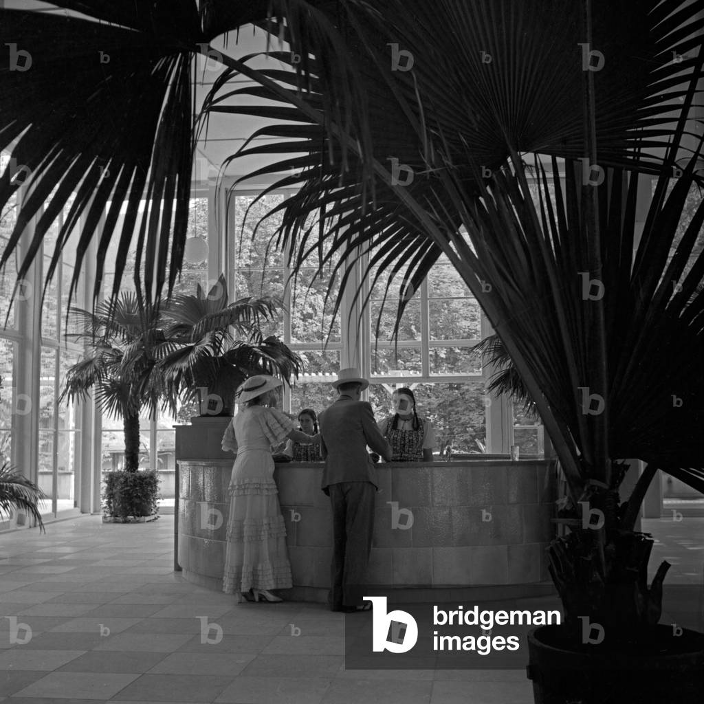Couple checking in at the reception of a spa resort hotel at Wildbad in Black Forest, Germany 1930s (b/w photo)