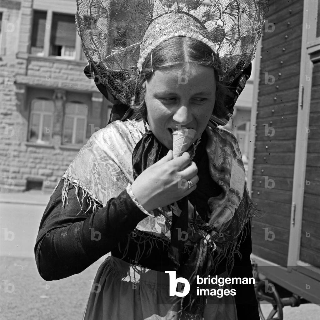 A woman with an ice cream at a traditional costume parade through the streets of Constance, Germany 1930s (b/w photo)