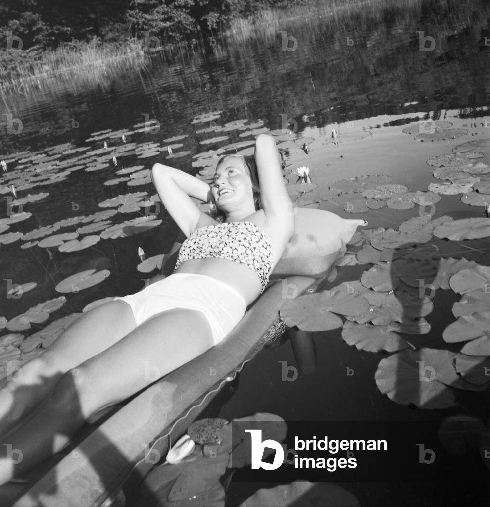 A young woman on an air matress on a lake in the Wachau area in Austria, Germany 1930s (b/w photo)