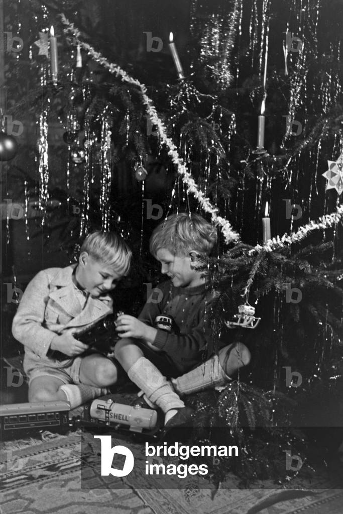 Two boys playing with the new model train under the christmas tree, Germany 1930s (b/w photo)