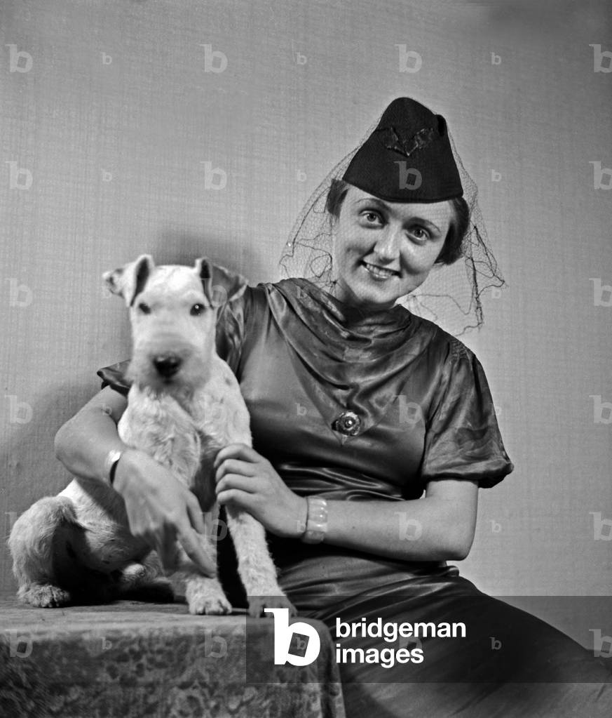 A lady and her dog pet at the photo studio in contemporary fashion, Germany 1930s (b/w photo)