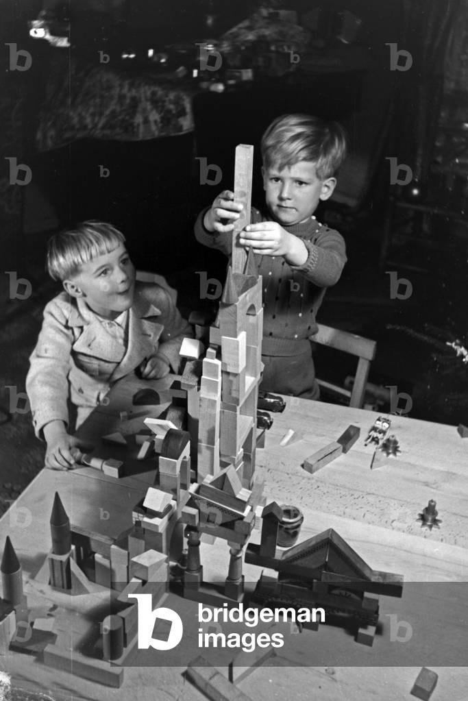 Two boys playing with the new set of toy blocks under the christmas tree, Germany 1930s (b/w photo)