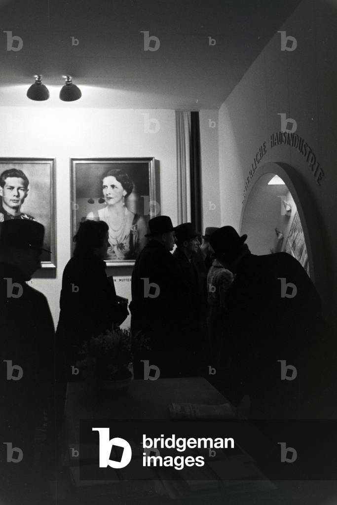 Visitors of the Leipziger Frühjahrsmesse at a Romanian stand with portraits of the Romanian King Michael I, and his mother Elena of Greece, Germany 1941 (b/w photo)