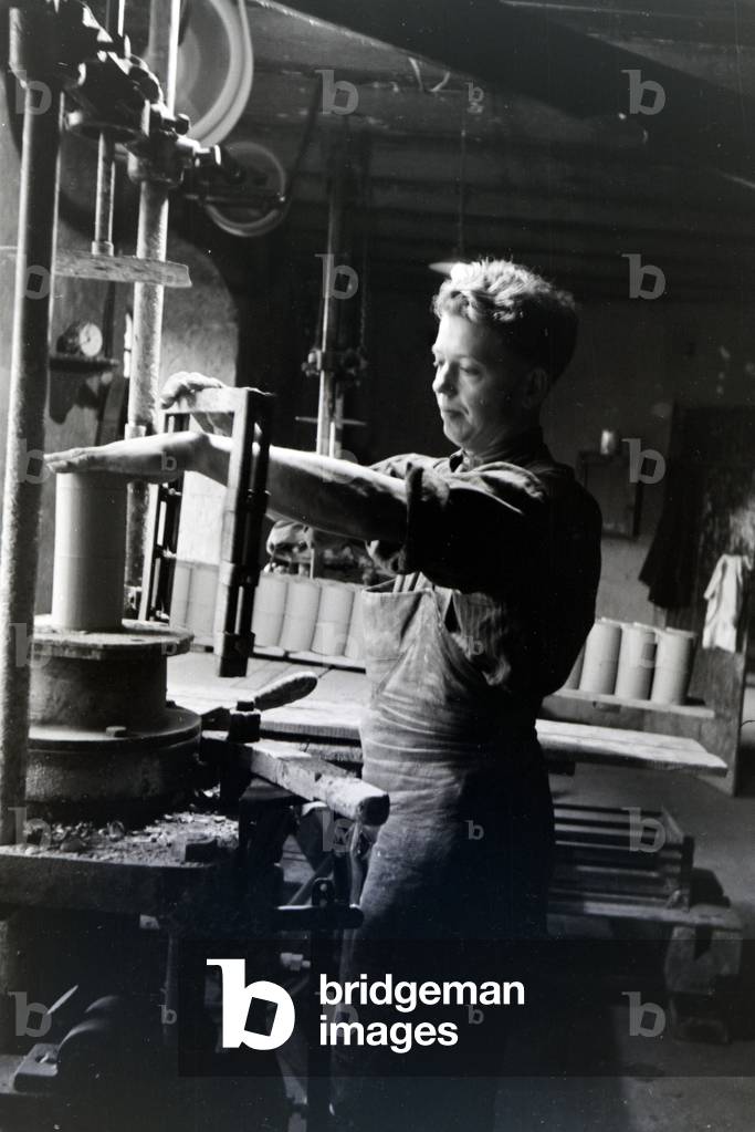 An employee of a stoneware factory in the Kannenbäckerland is cutting raw clay into smaller pieces, Germany 1930s (b/w photo)
