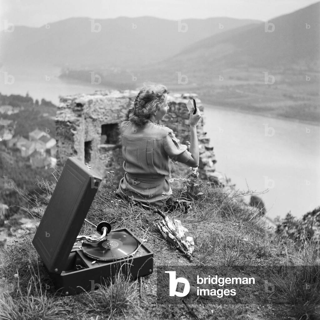 A young woman sitting in a lawn and listening to the lastest hits from her Electrola gramophone, Germany 1930s (b/w photo)