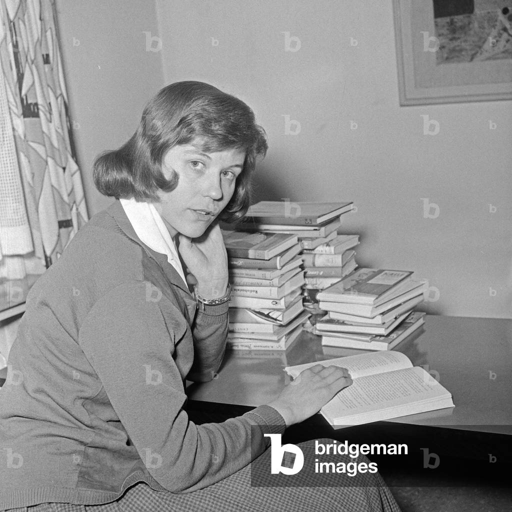 A young woman with a pile of books sitting at a table, Germany 1950s