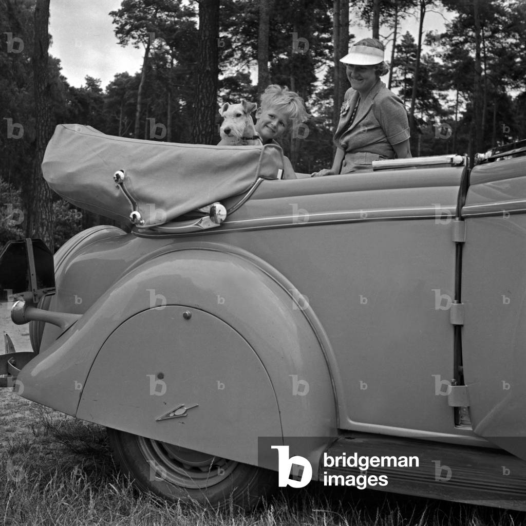 A young woman, a little boy and a fox terrier looking forward for camping, Germany 1930s (b/w photo)