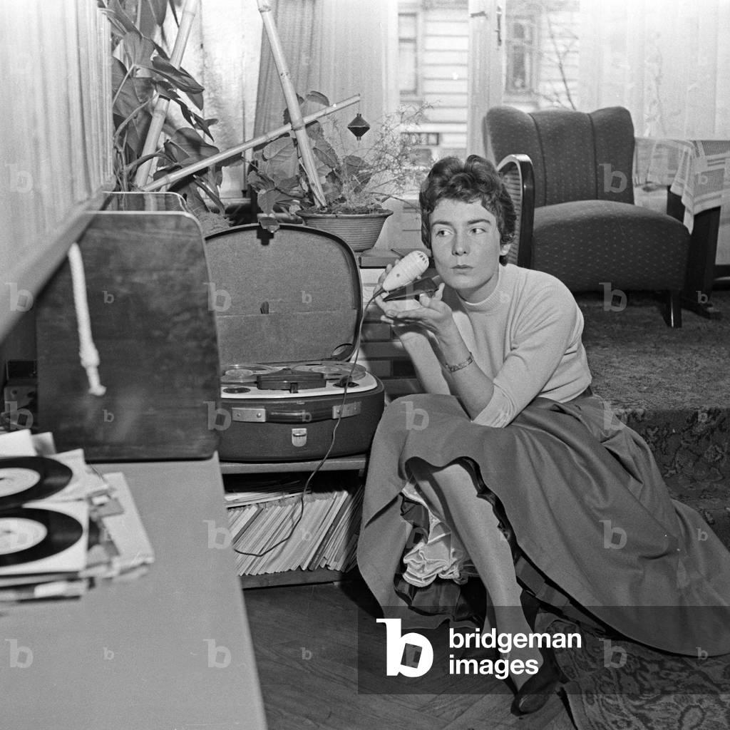 German schlager singer Melitta Berg sitting on the floor of a living room with a microphone and a reel to reel tape recorder, Germany 1950s