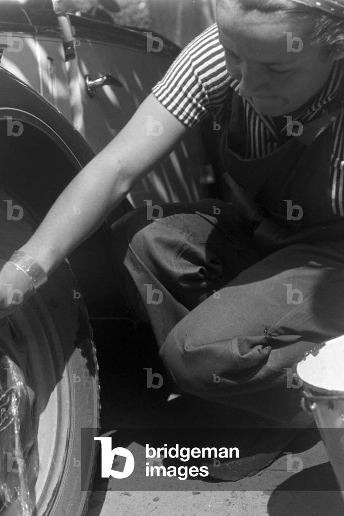 A young woman washing a Ford model Eifel, Germany 1930s (b/w photo)