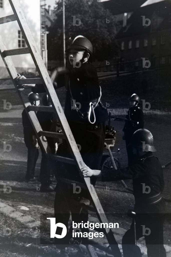 A boy of the junior firefighters is climbing up a ladder during a firefighter training, Germany 1930s (b/w photo)