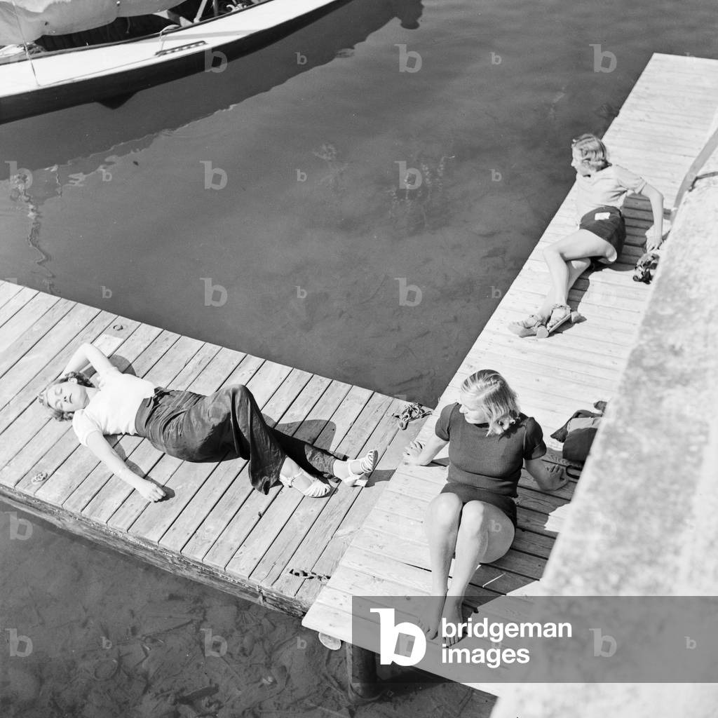 Three young women on a boardwalk on the shore of a lake in the Wachau area in Austria, Germany 1930s (b/w photo)