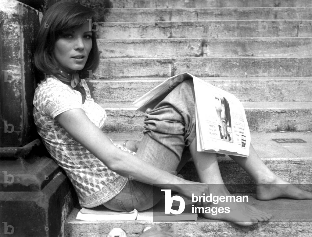 German actress Iris Berben sitting on a stair reading newspaper, 1970s