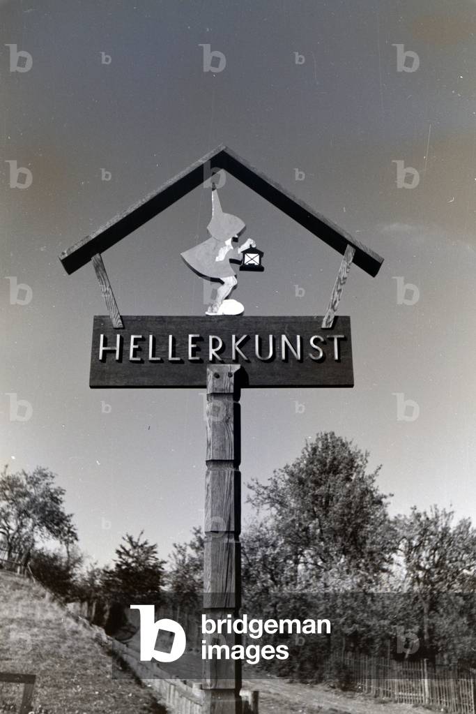 The nameplate of the Heller Kunst workshops in the Eifel with the fairytale motive of a dwarf with a lantern, Germany 1930s (b/w photo)