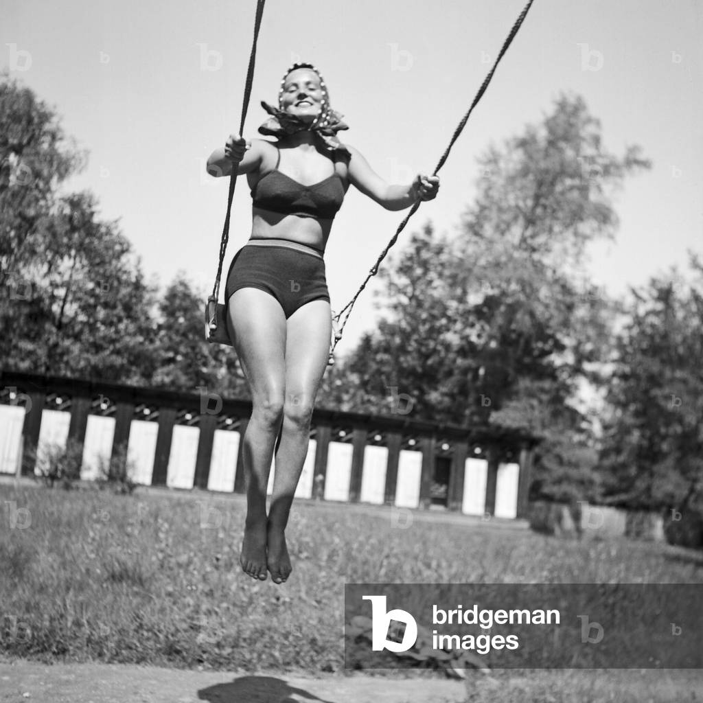 A young woman wearing a bikini on a swing on a playground in the Wachau area in Austria, Germany 1930s (b/w photo)