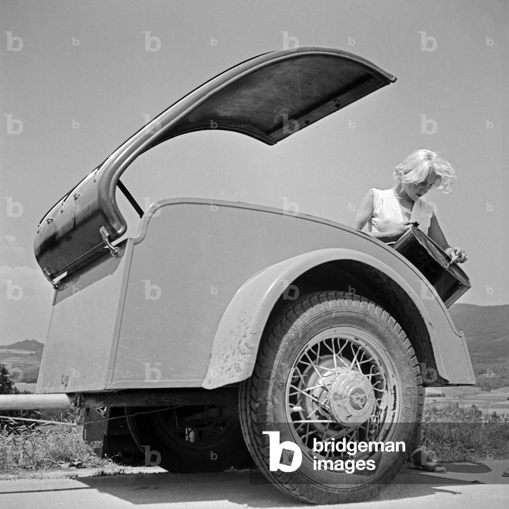 A woman taking camping equipment out of a trailer if a Ford V8, Germany 1930s (b/w photo)