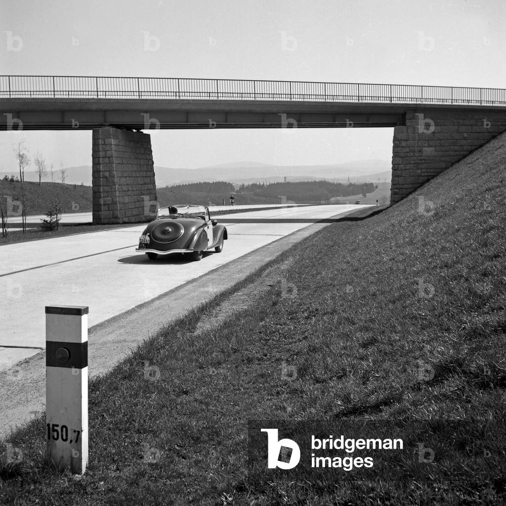 A Ford model Eifel under a bridge at the Reichsautobahn highway, Germany 1930s (b/w photo)