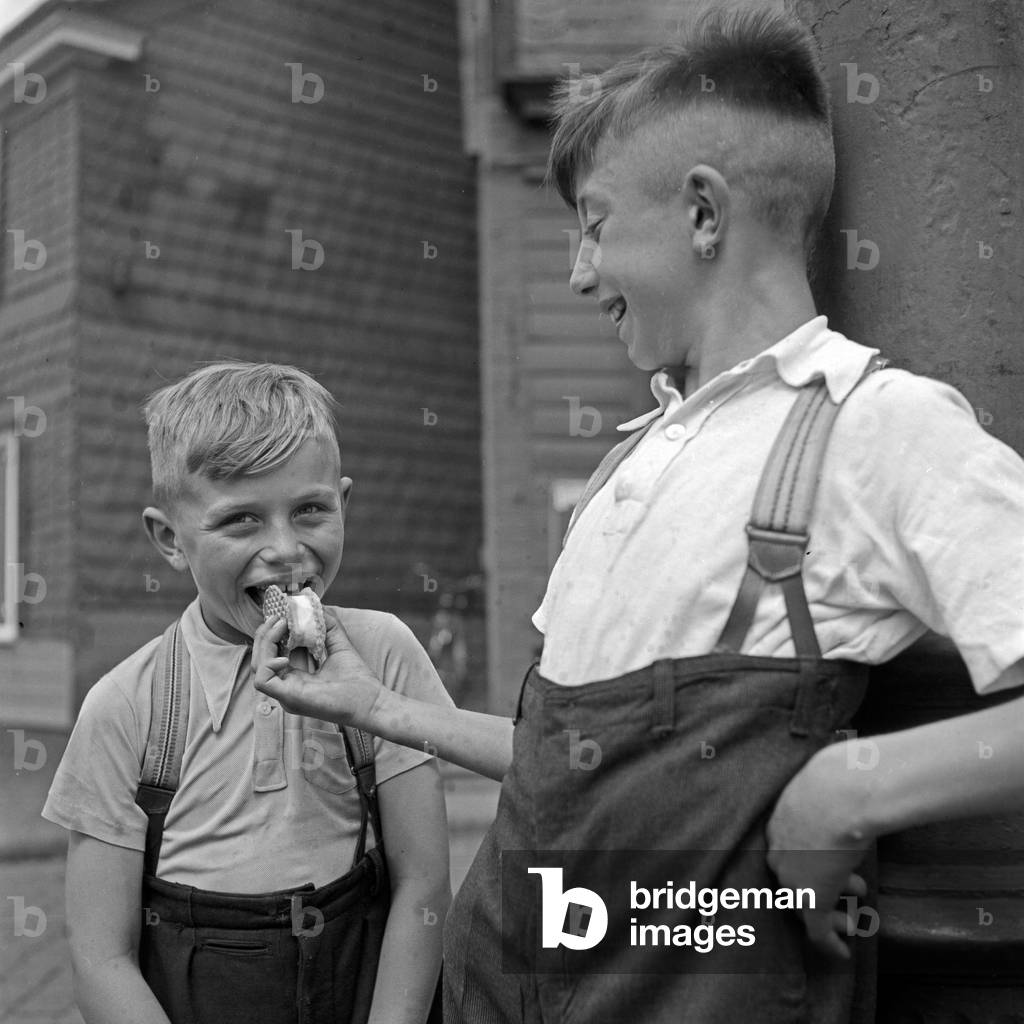 A boy sharing his ice cream wafer with a friend, Germany 1930s (b/w photo)